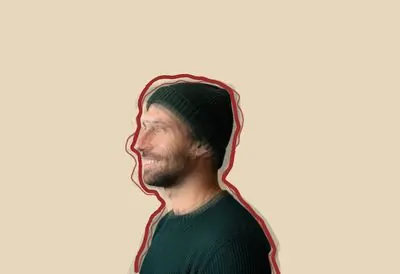 رجل مبتسم يرتدي قبعة صوفية، يظهر من الجانب، وحوله نسخ باهتة منه مزاحة قليلًا، ويحيط به خط أحمر مرسوم باليد
