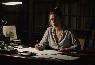 A researcher at her desk late at night, frowning at survey printouts under a lamp